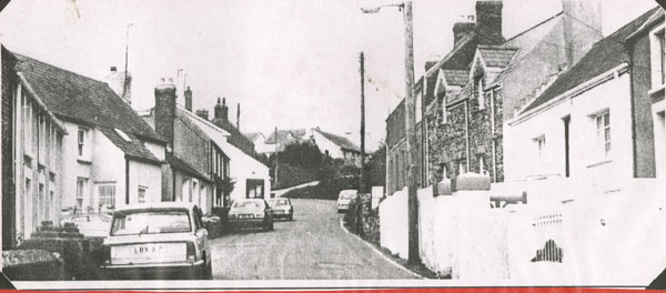 Copy of a photograph looking up the hill on Main Street Llangwm showing cars
